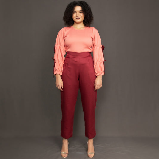 Model wearing high waist burgundy trousers and salmon pink long sleeve top by Kim Dave 