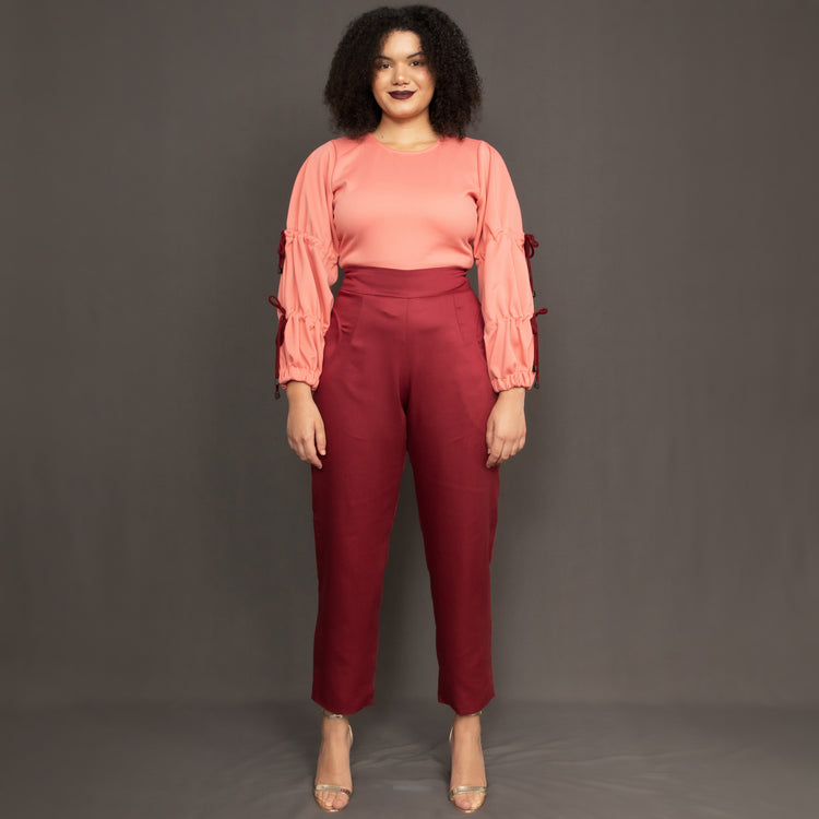 Model wearing high waist burgundy trousers and salmon pink long sleeve top by Kim Dave 