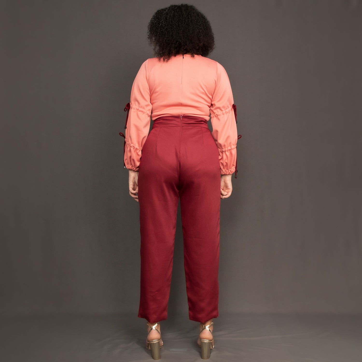 Model wearing high waist burgundy trousers and salmon pink long sleeve top by Kim Dave